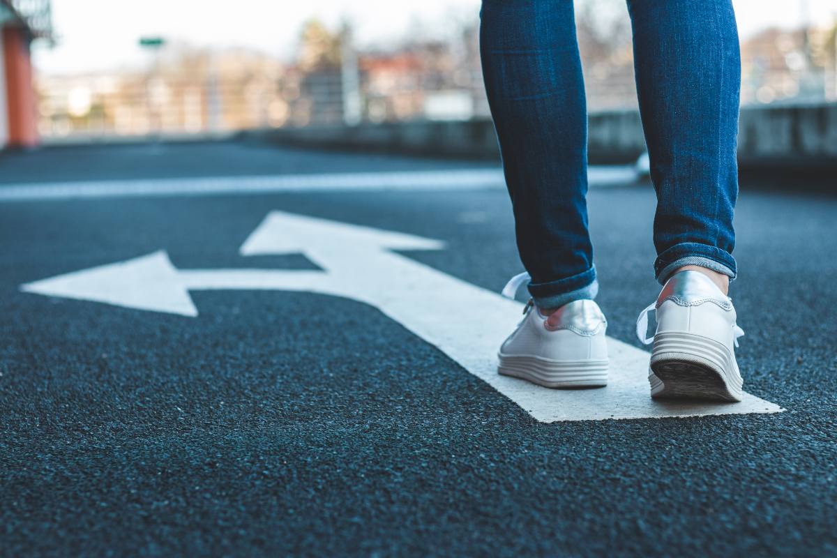 Ragazza cammina con jeans e scarpe bianche su segnale stradale di un bivio disegnato a terra