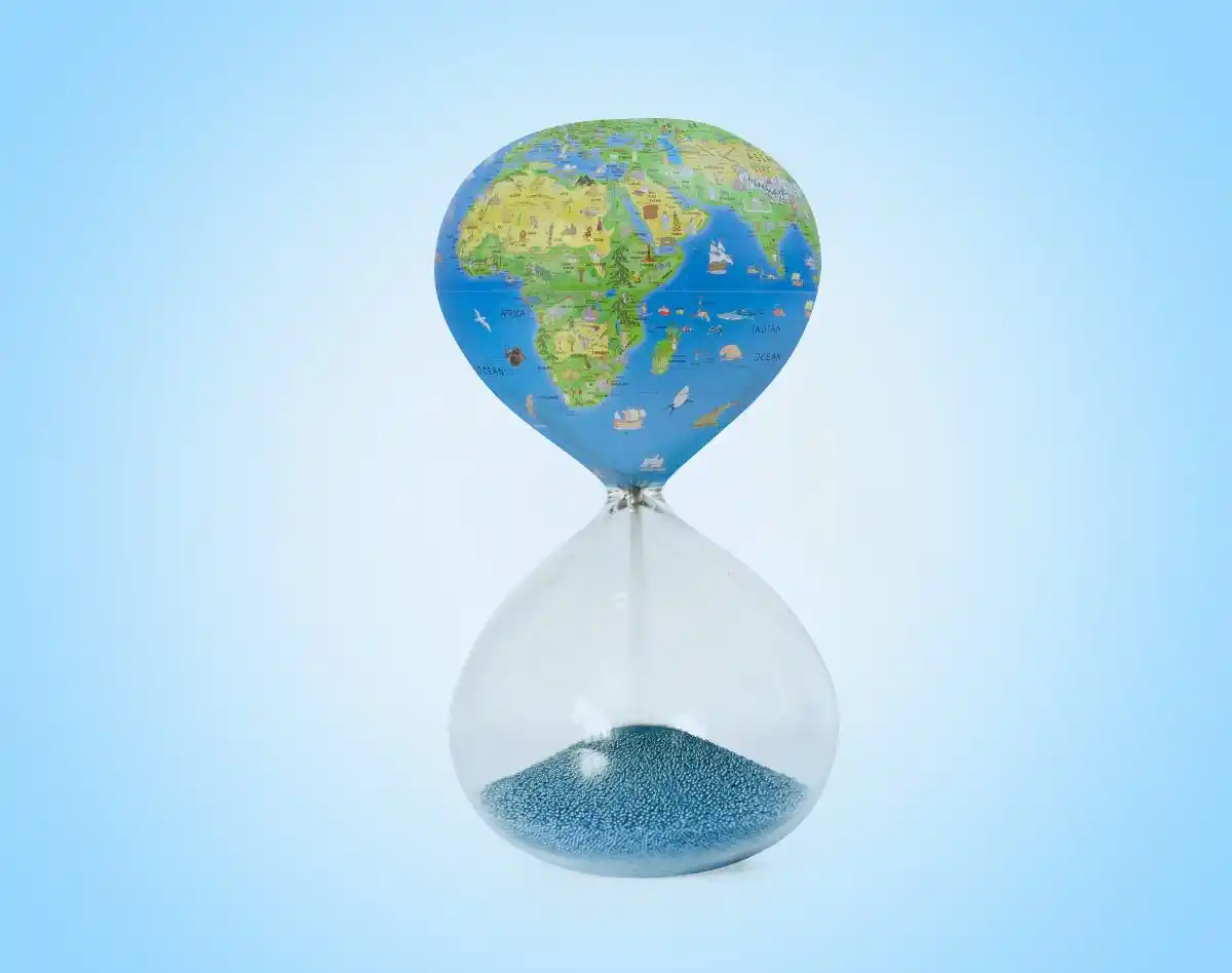 Clessidra con mezza mappa del mondo sopra, sabbia blu sotto, sfondo azzurro.