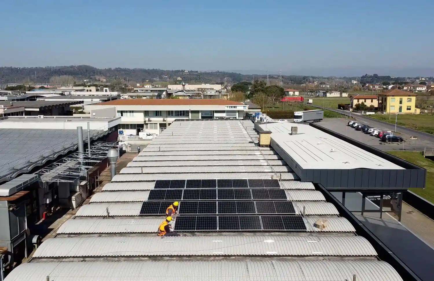 Operai installano pannelli solari su un tetto industriale in area urbana.