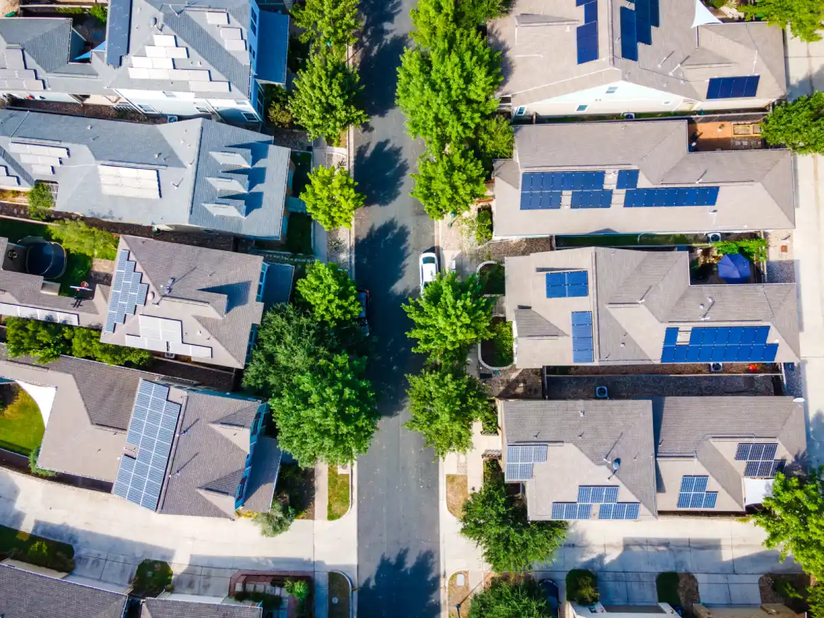 Quartiere residenziale visto dall'alto con case dotate di pannelli solari sui tetti e alberi lungo la strada.