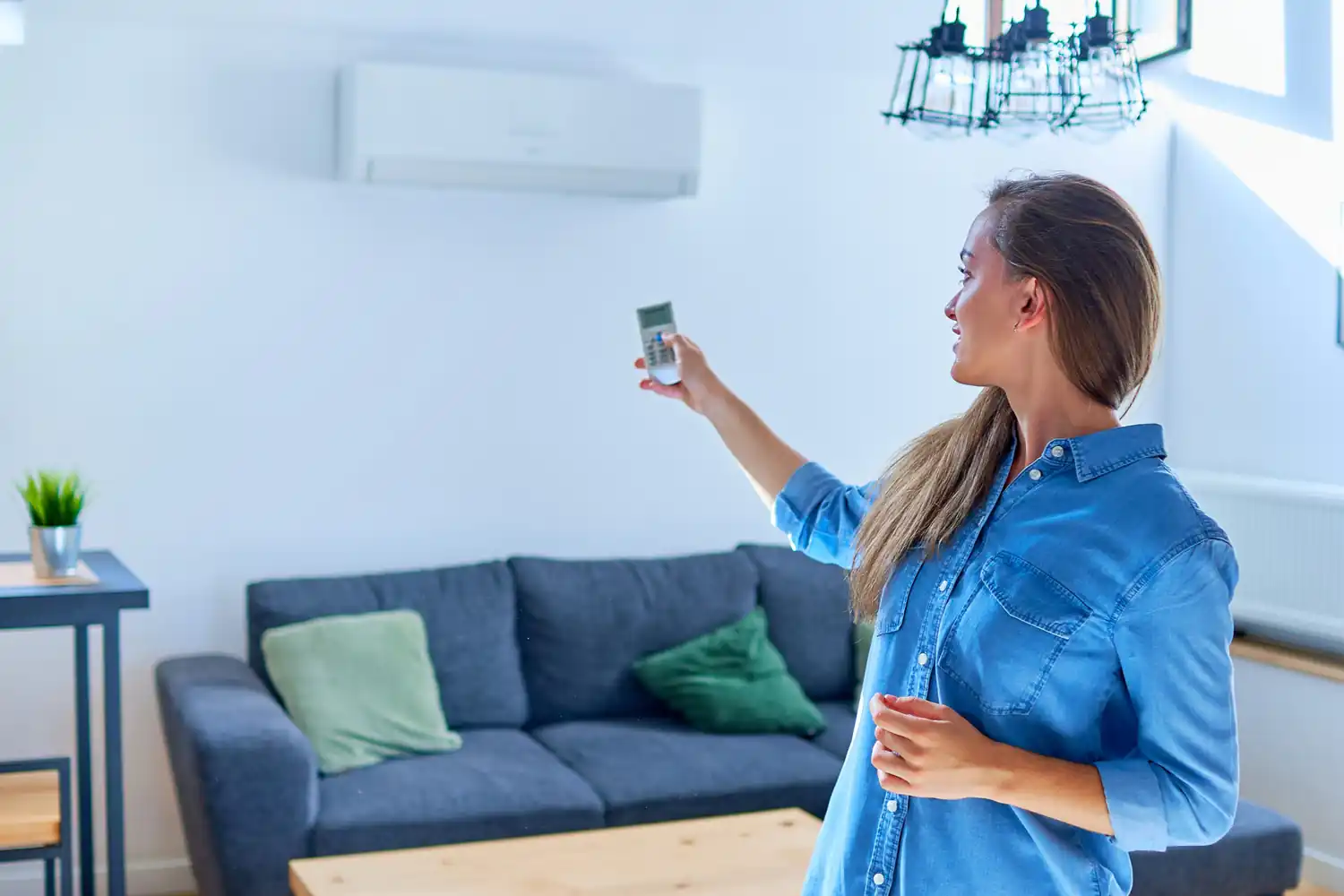 Donna con telecomando regola condizionatore in soggiorno moderno con divano e pianta.