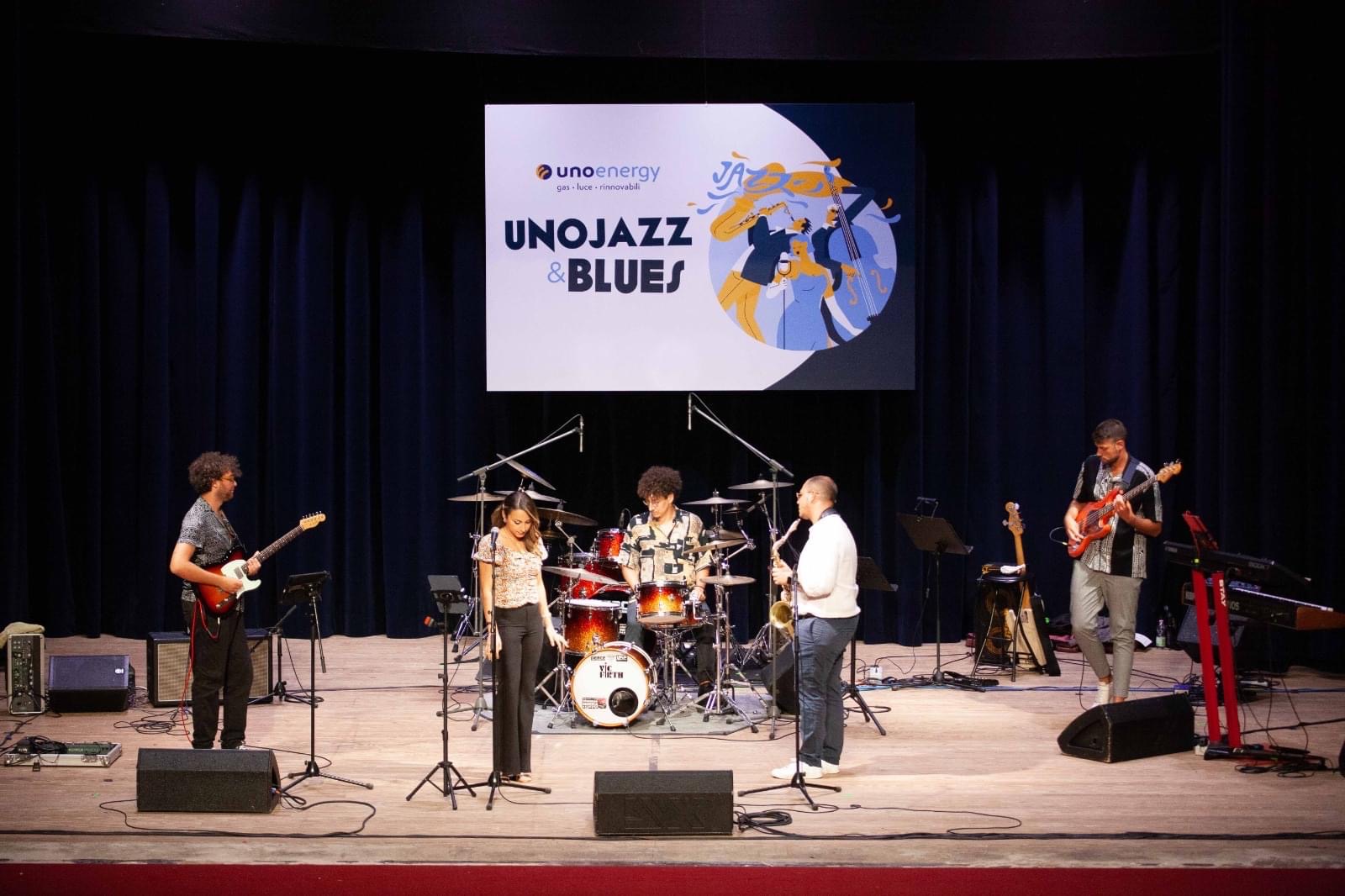 Band suona musica jazz dal vivo al festival UnoJazz & Blues con chitarra, sax, batteria e basso sul palco.