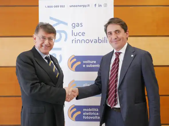 Due uomini in abito si stringono la mano davanti a un banner di un'azienda energetica.