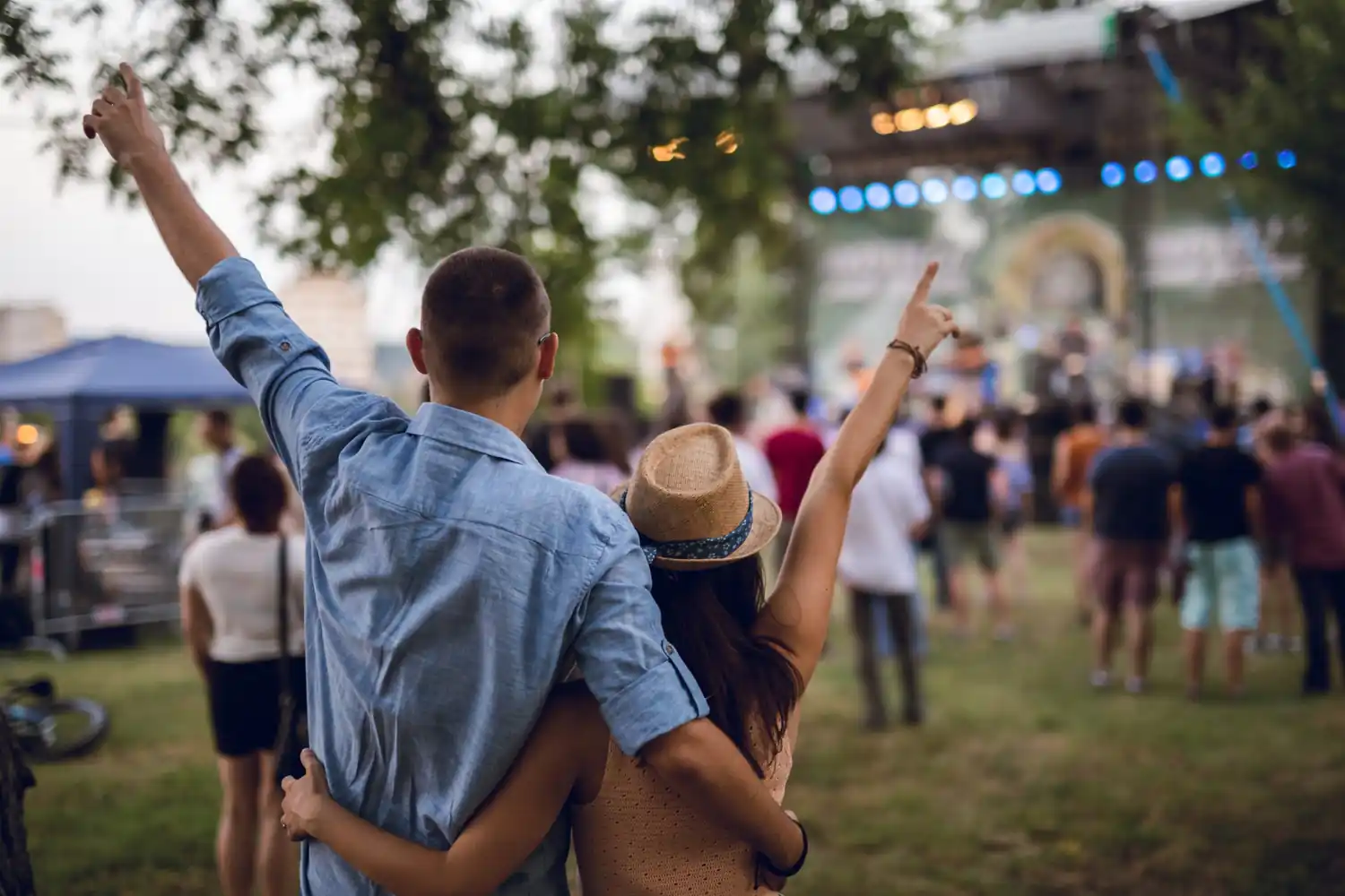 Due persone abbracciate al concerto all'aperto, pubblico davanti al palco illuminato.