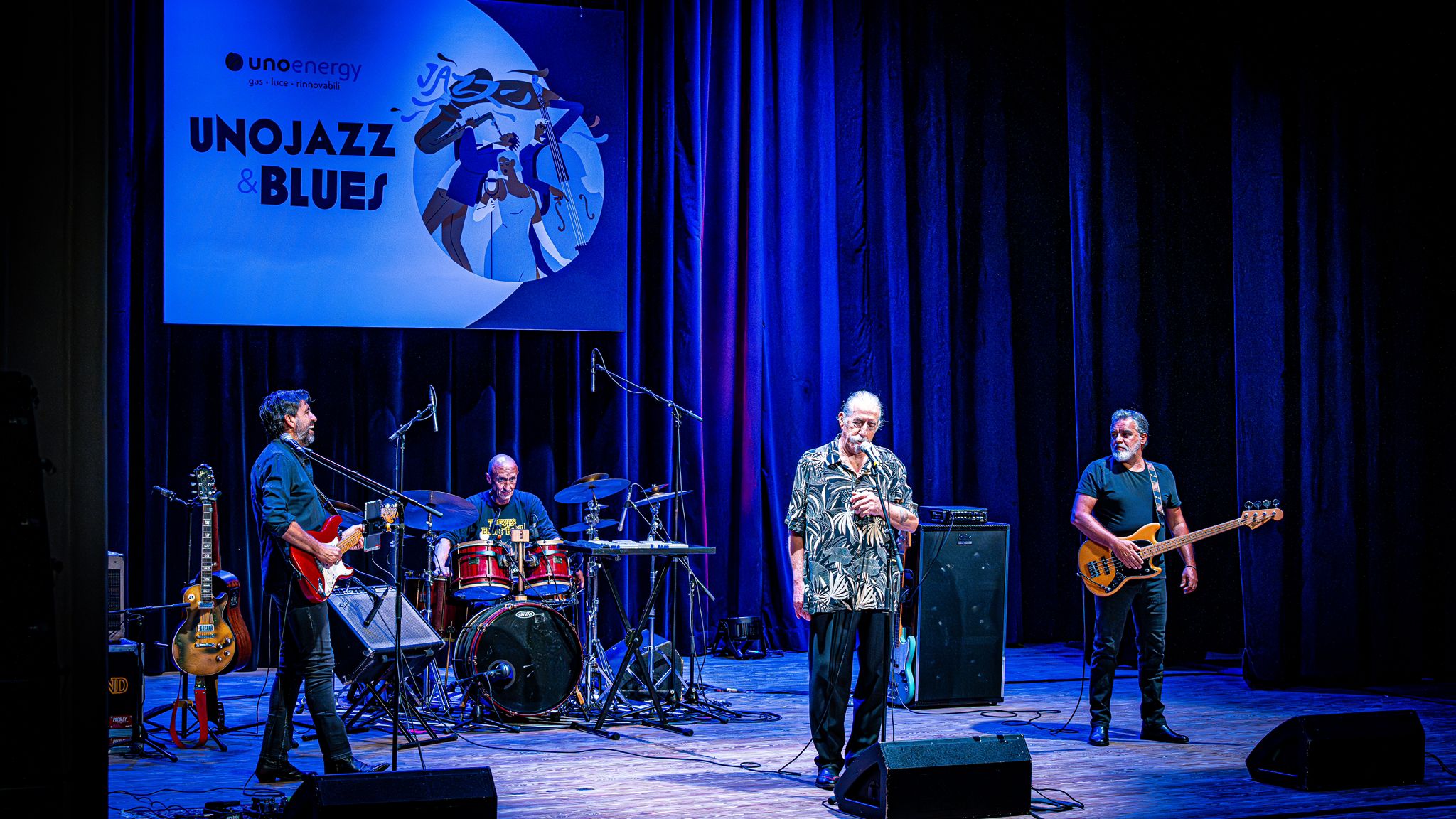 Concerto jazz con quattro musicisti su palco blu, banner Unojazz & Blues sullo sfondo.