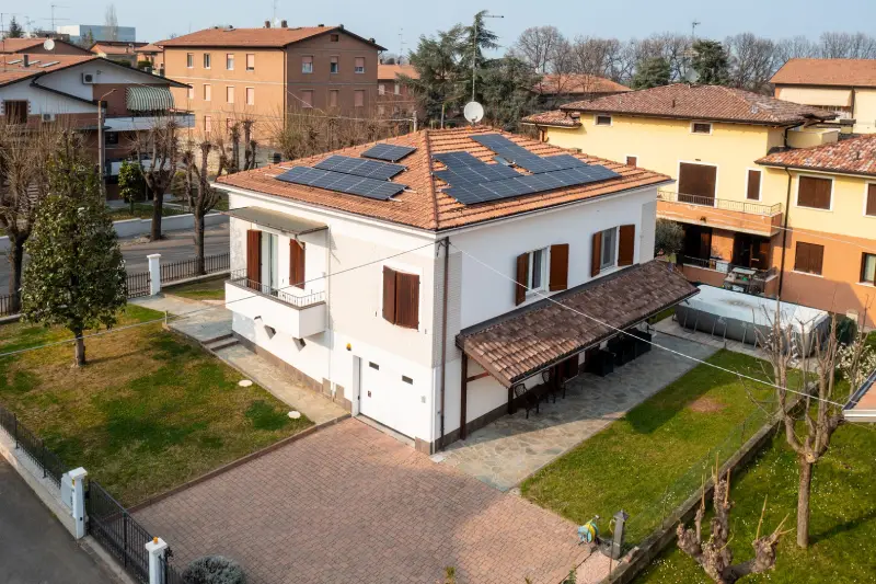 Casa moderna con pannelli solari sul tetto, giardino curato e vialetto pavimentato in quartiere residenziale.
