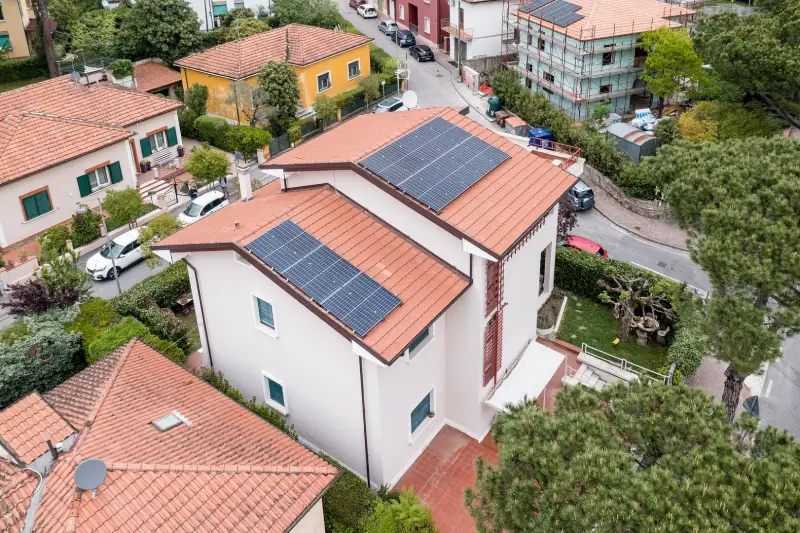 Casa con tetto in tegole rosse e pannelli solari, situata in un quartiere residenziale con giardino.