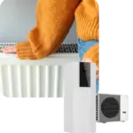 Donna con maglione arancione tocca un radiatore bianco, accanto a una pompa di calore.