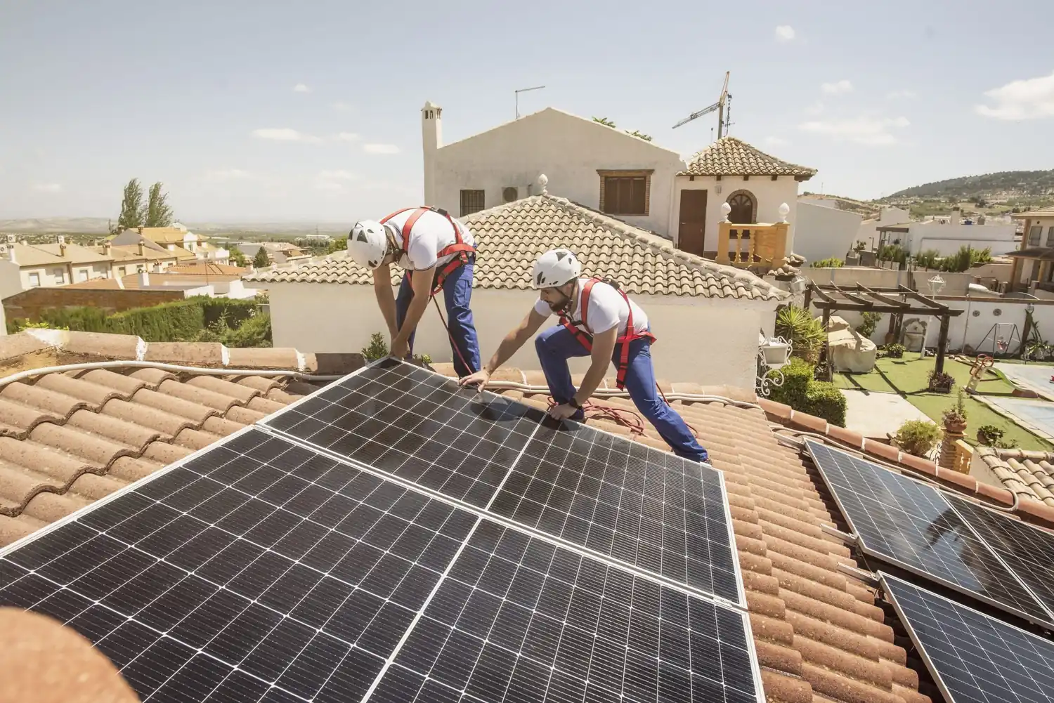 Installazione di pannelli solari su tetto di casa da parte di tecnici con caschi e imbracature.