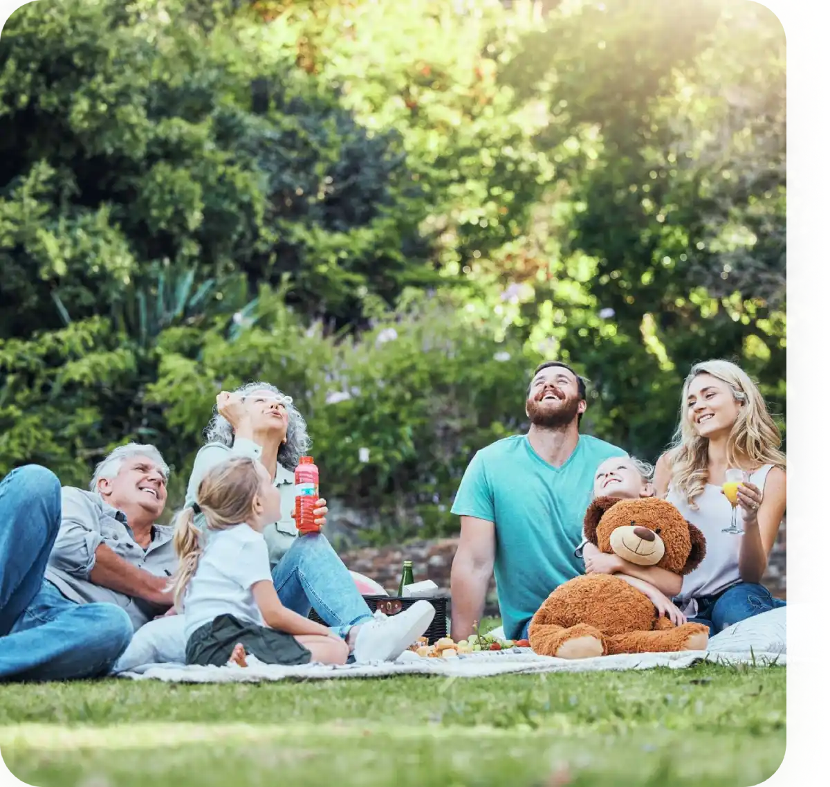 Famiglia felice seduta su un prato durante un picnic all'aperto, circondata da alberi verdi.