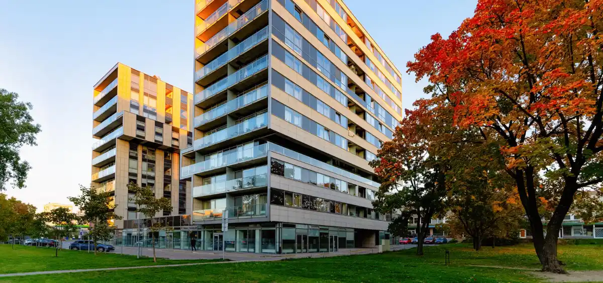 Edificio residenziale moderno con vetrate, circondato da alberi in autunno, cielo sereno.
