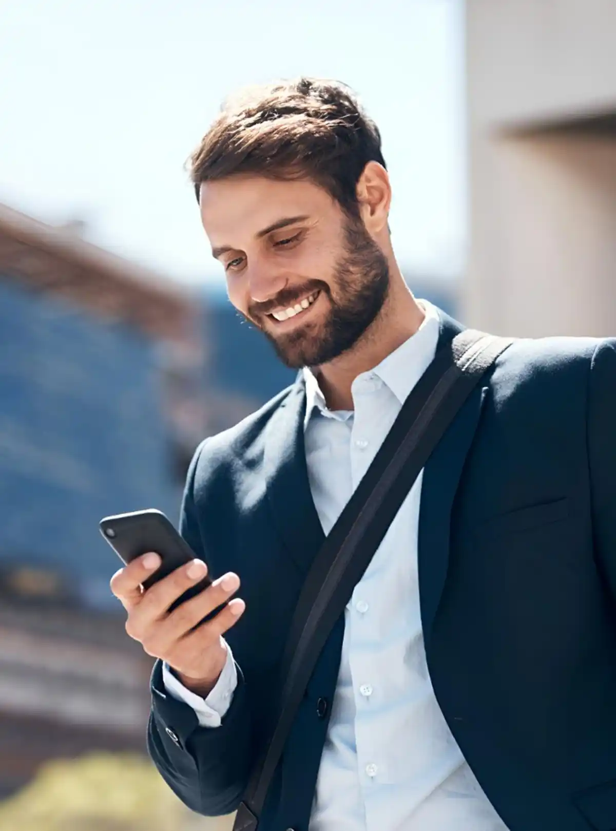 Uomo in abito business sorride mentre guarda il telefono all'aperto.