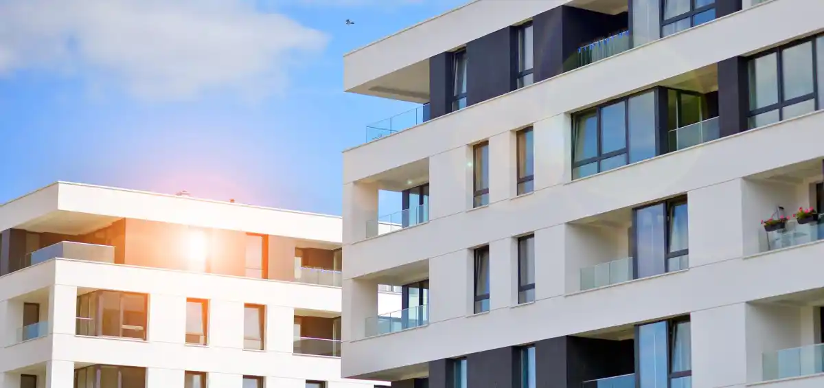 Moderni edifici residenziali con finestre ampie e balconi, cielo blu e sole splendente.