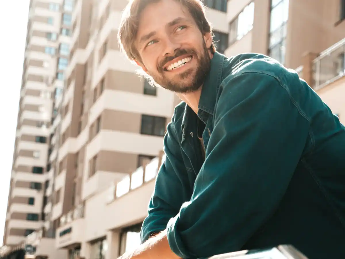 Uomo sorridente in camicia verde davanti a edifici alti, ripreso in ambiente urbano.