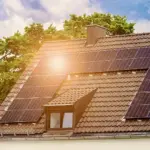 Tetto con pannelli solari sotto il sole, circondato da alberi e cielo nuvoloso.