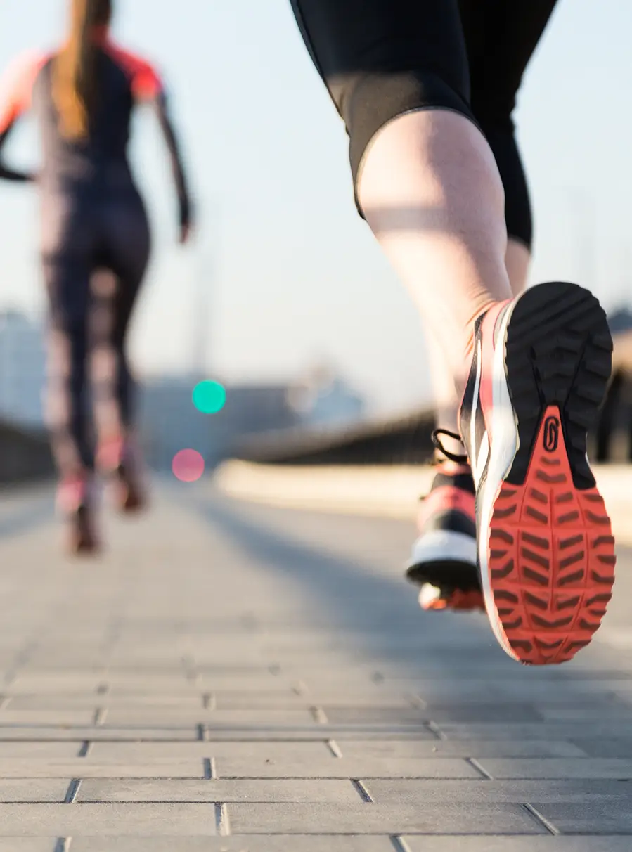 Due persone corrono su un marciapiede in città, scarpe da ginnastica visibili.