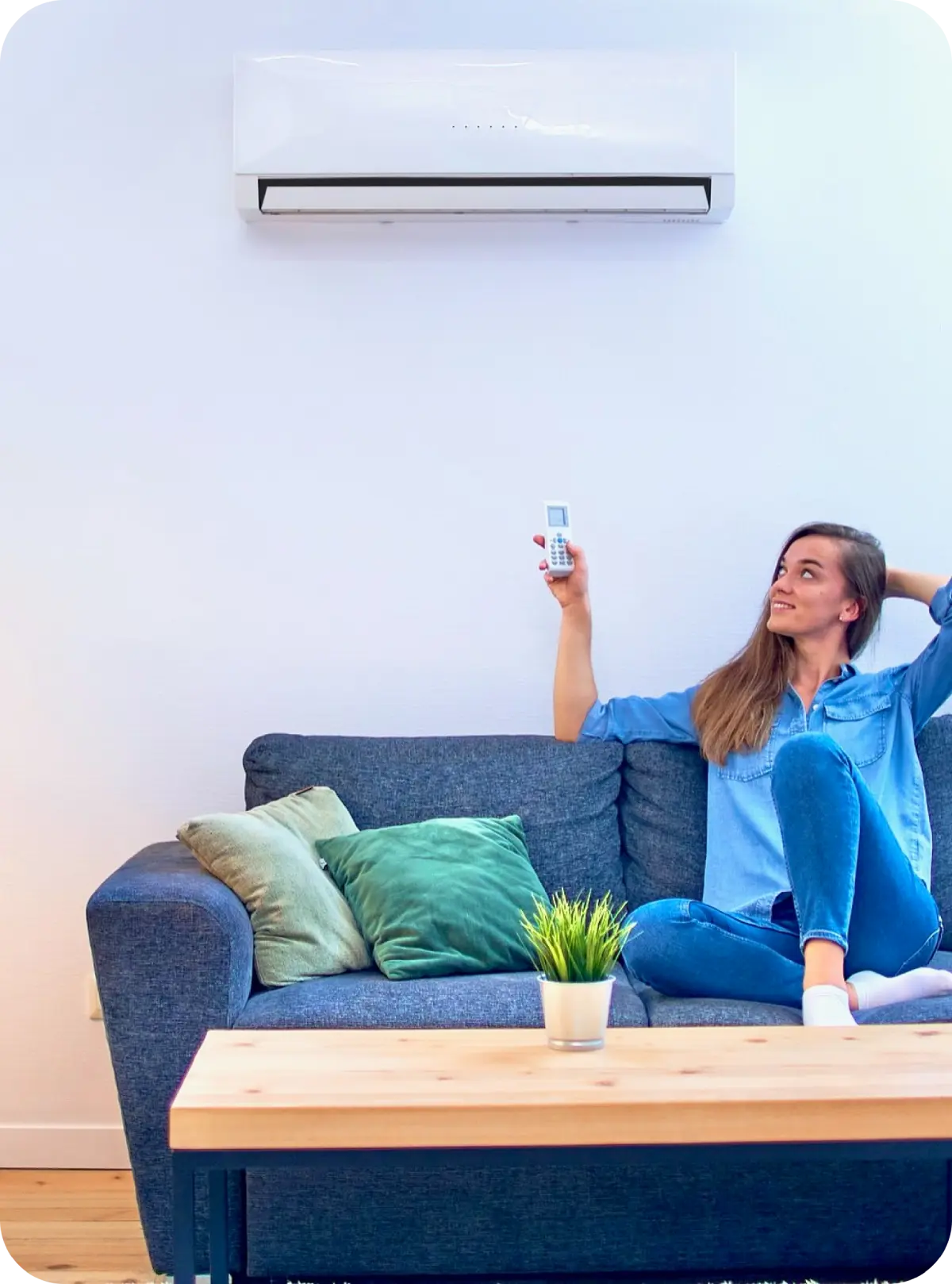 Donna sul divano usa il telecomando per climatizzatore montato a muro, pianta su tavolino davanti a lei.