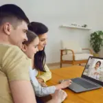 Famiglia partecipa a videochiamata con professionista su laptop in soggiorno luminoso.