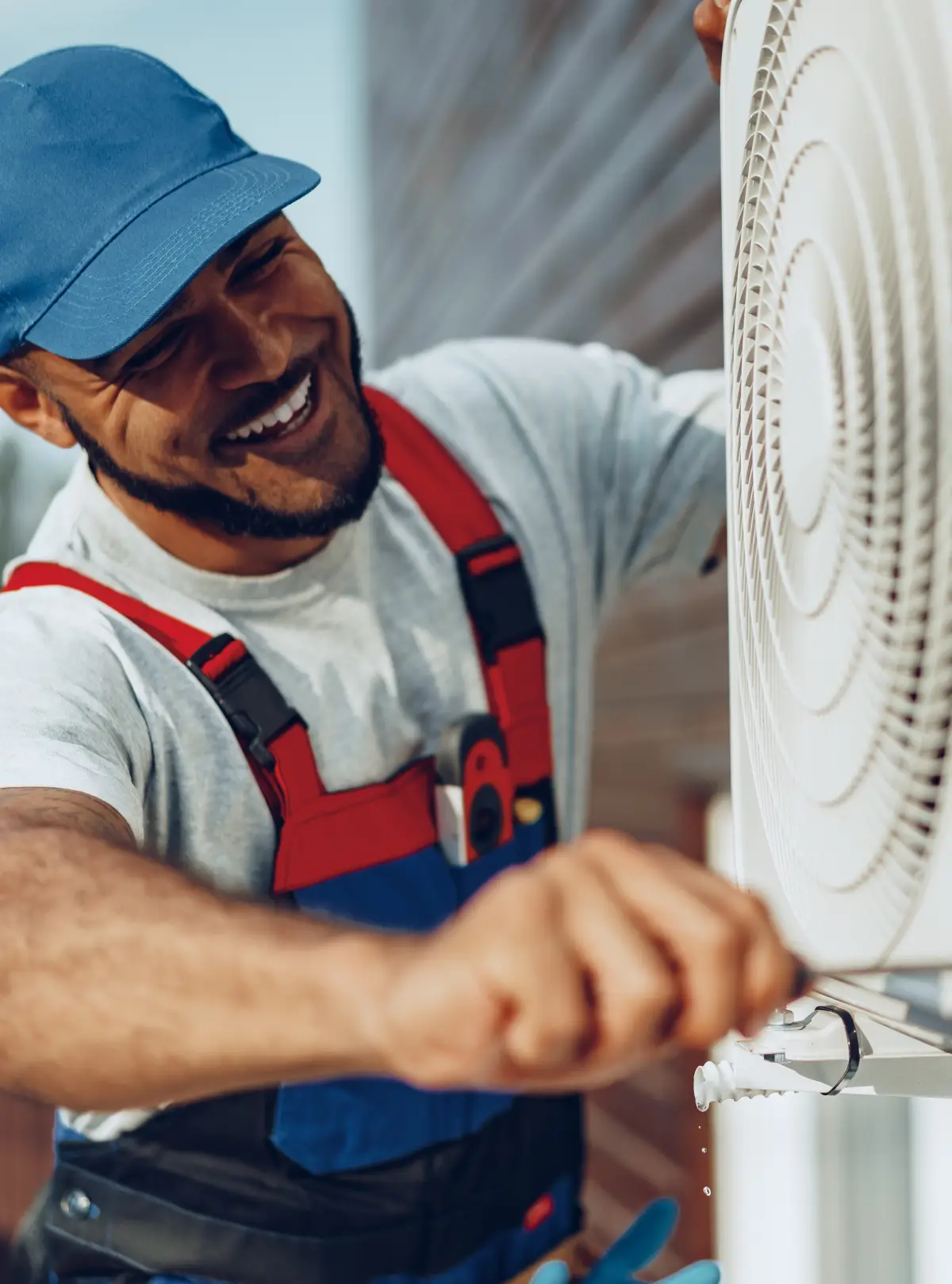 Tecnico del condizionatore con cappello blu e tuta lavora su un'unità esterna.