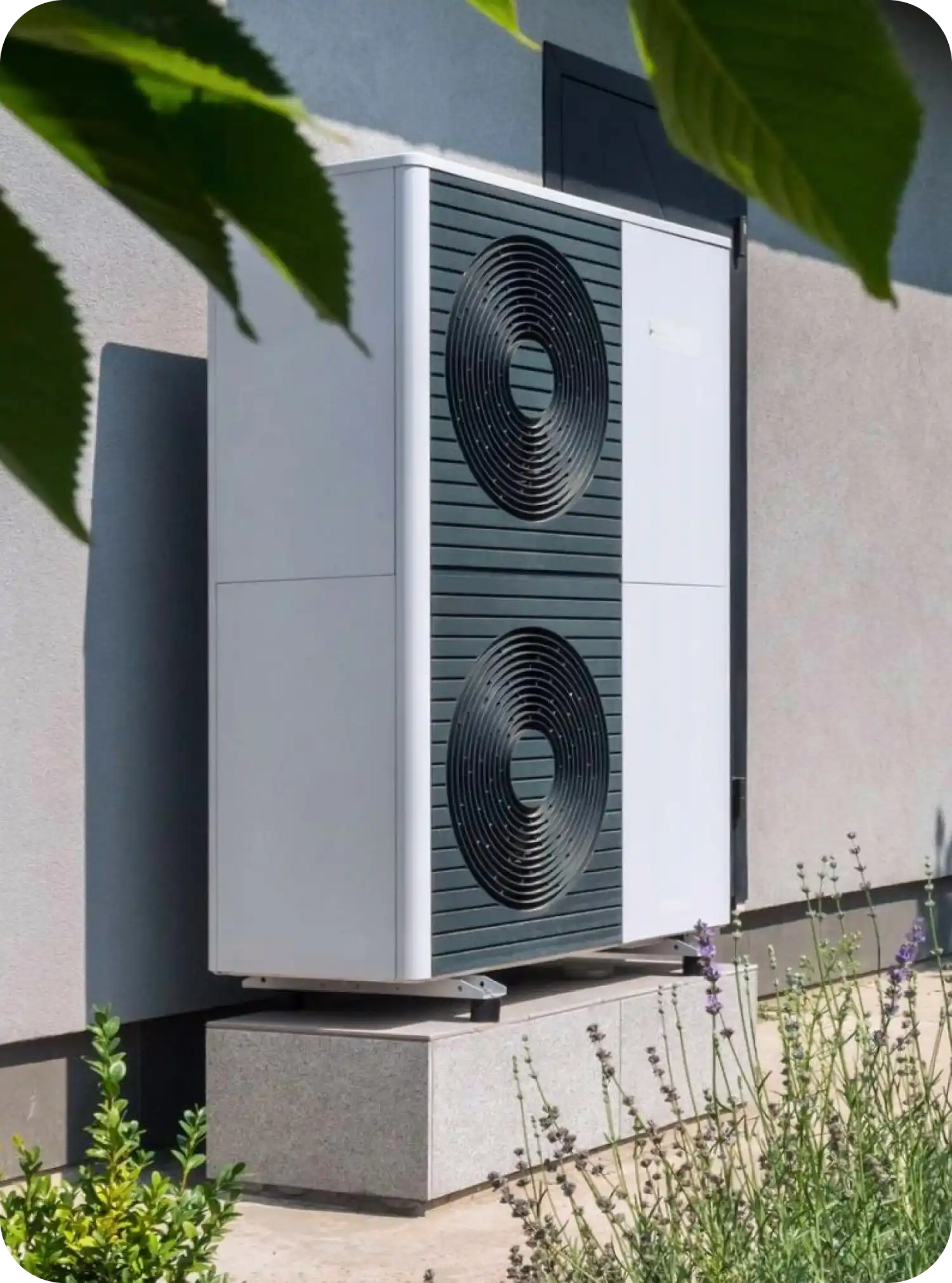 Pompa di calore esterna montata sulla parete di un edificio, circondata da piante.