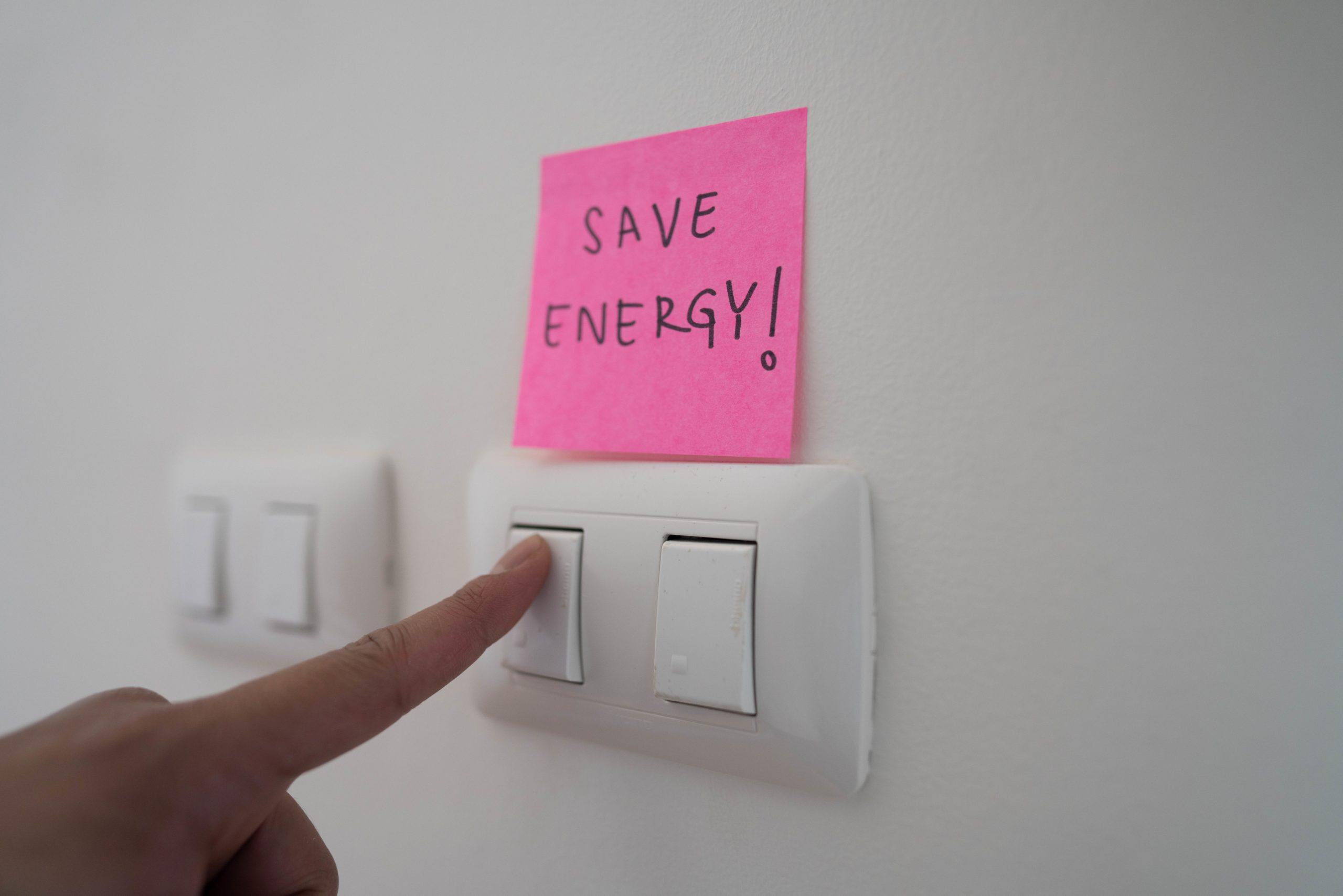 Dito preme interruttore luce, adesivo rosa con scritta Save Energy per promuovere il risparmio energetico.