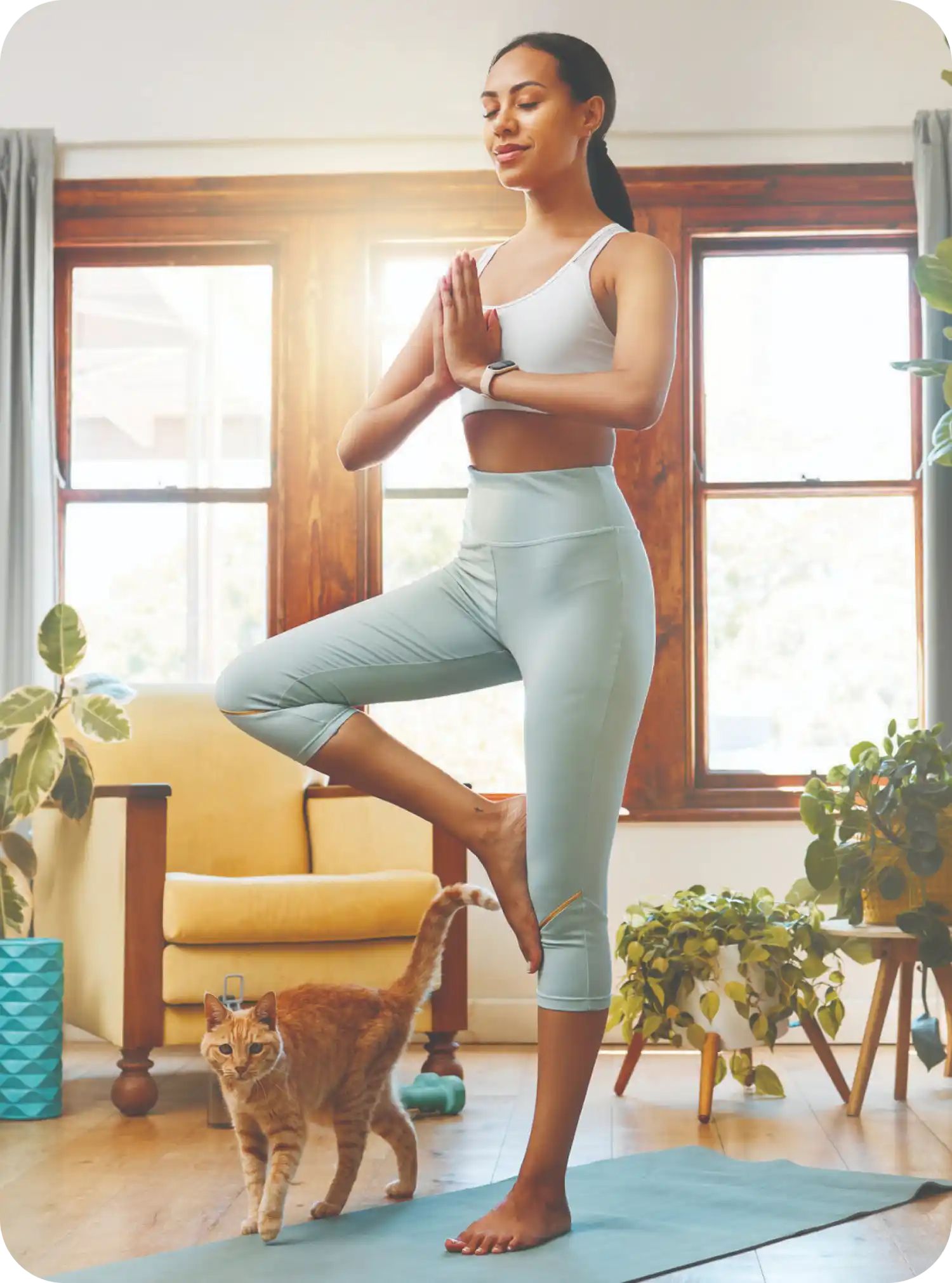 Donna pratica yoga in soggiorno con gatto, circondata da piante, indossa abiti sportivi chiari.