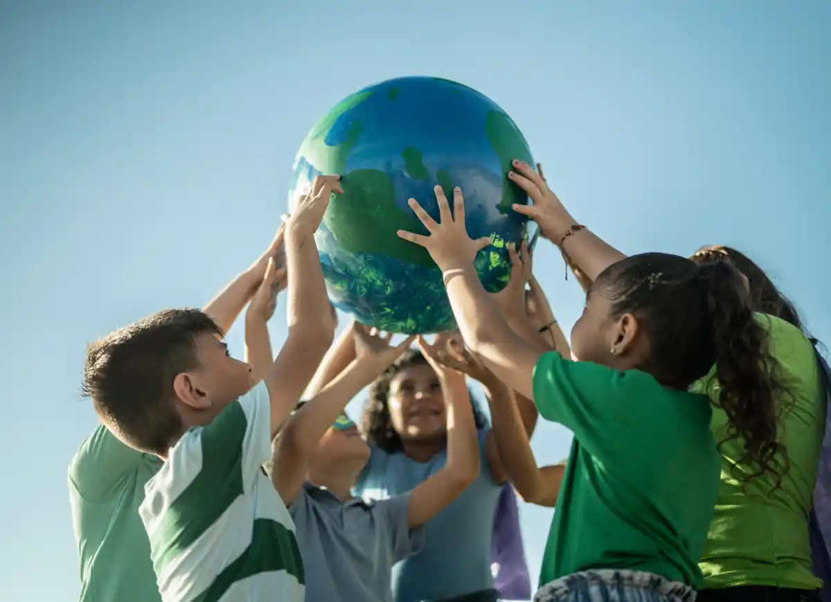 Bambini sollevano un globo terrestre gonfiabile sotto il cielo blu, simboleggia la collaborazione globale.