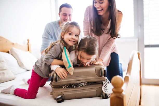Famiglia felice prepara il bagaglio sul letto. Due bambine aiutano a chiudere la valigia. Preparativi per viaggio.