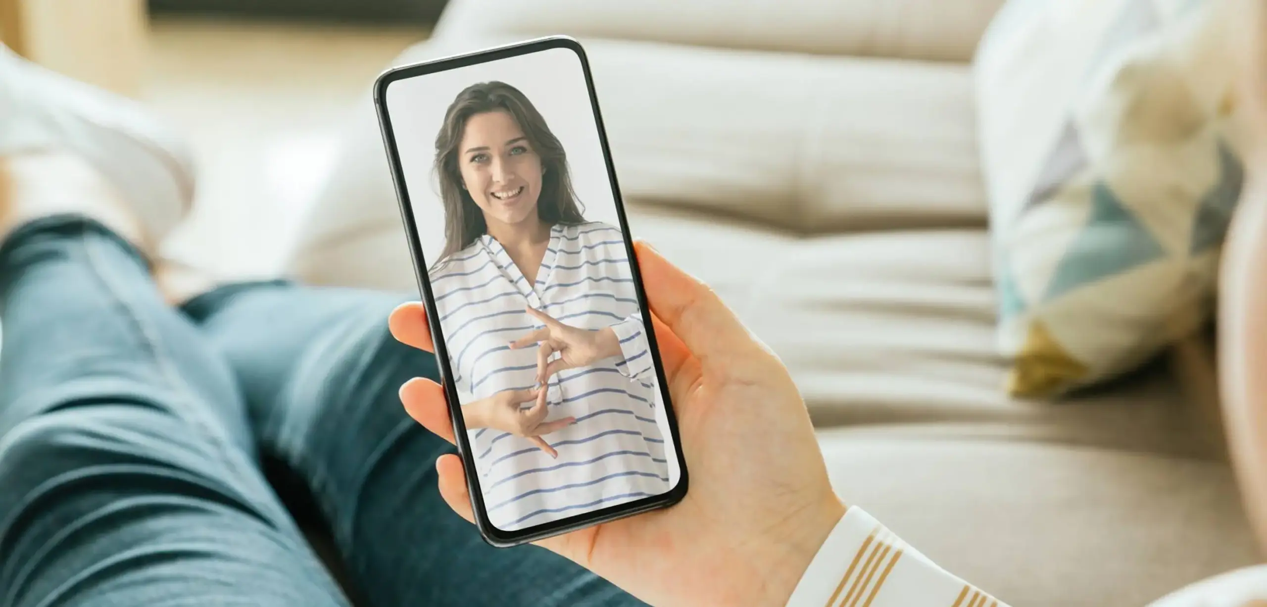 Utente guarda videochiamata in lingua dei segni su smartphone da divano.