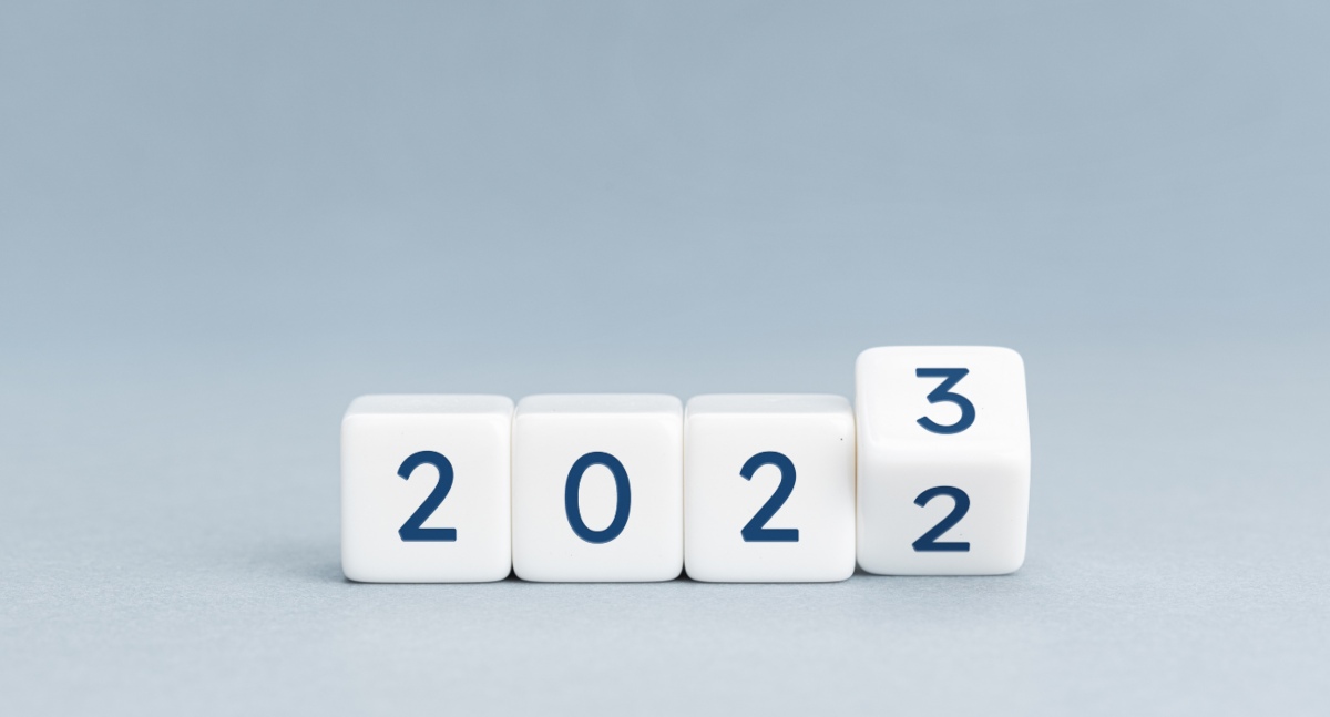 Dadi bianchi con numeri blu mostrano transizione dall'anno 2022 al 2023 su sfondo grigio chiaro.