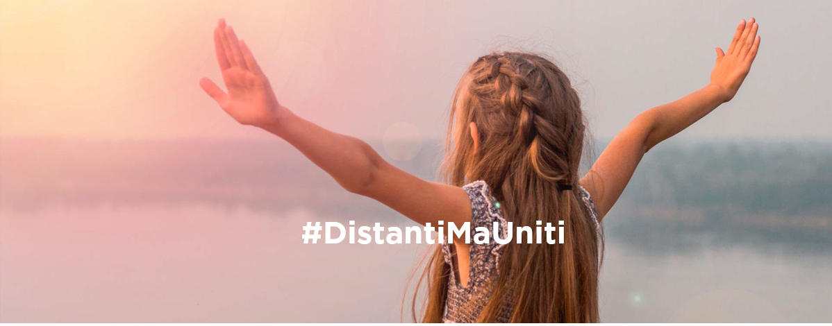 Bambina di spalle con braccia aperte, hashtag #DistantiMaUniti, sfondo naturale sfocato.