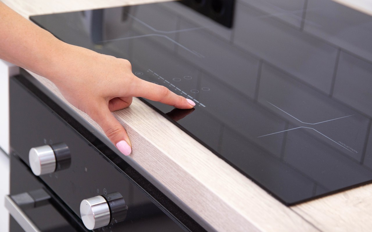 Dito che tocca il pannello di controllo di un piano cottura a induzione moderno in cucina.