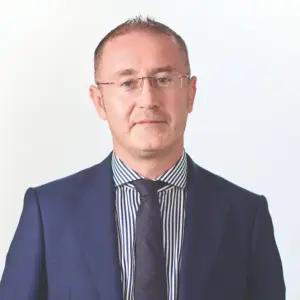 Ritratto di uomo in abito blu e cravatta scura, camicia a righe, sfondo bianco.