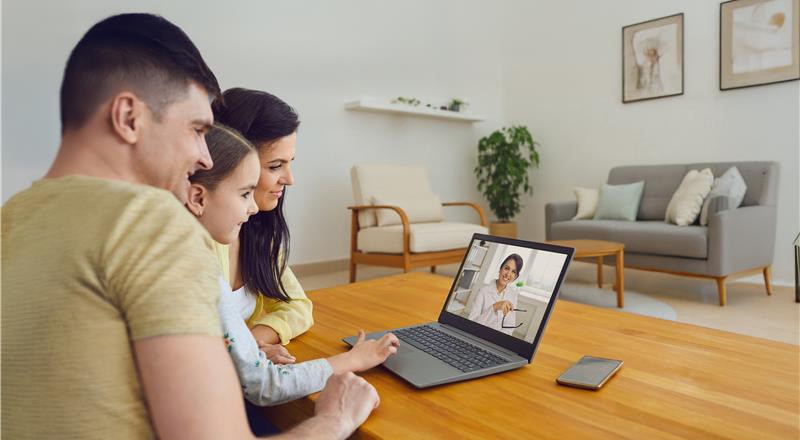 Famiglia fa videochiamata con medico al laptop, seduti al tavolo in salotto.