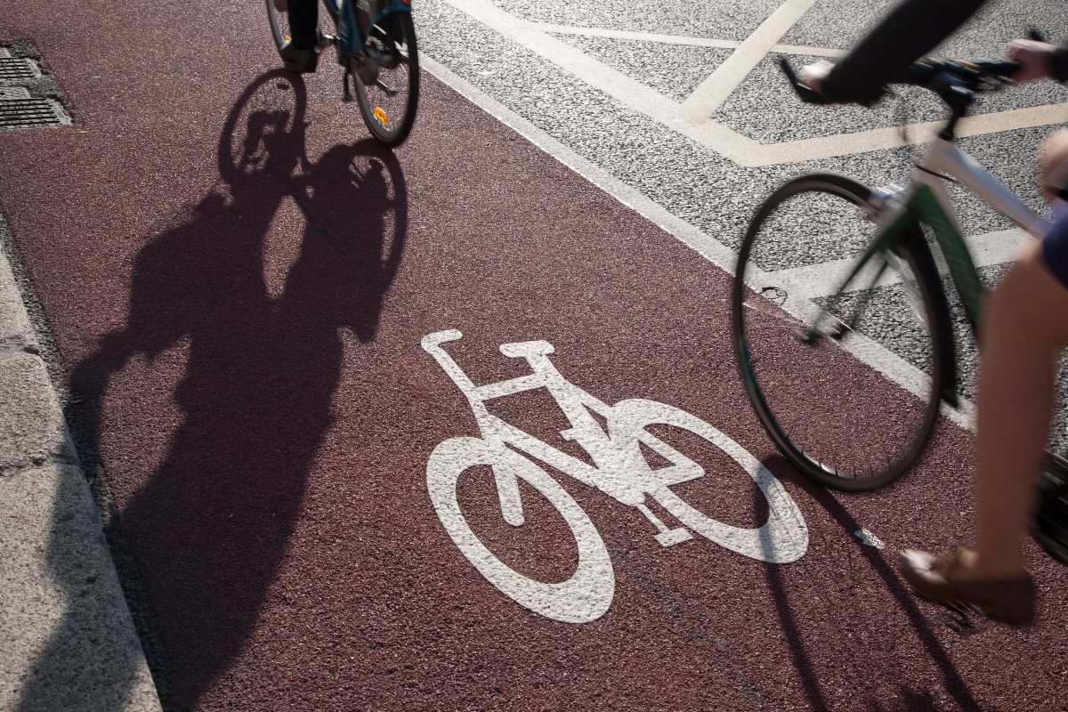 Due ciclisti su pista ciclabile rossa con simbolo bicicletta bianco, ombra visibile.