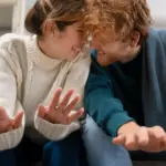 Due persone sorridenti si toccano la fronte, indossano maglioni e sono sedute vicine.