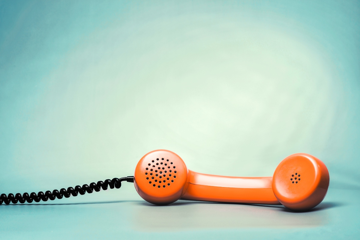 Cornetta telefonica arancione vintage su sfondo turchese chiaro con cavo nero a spirale.