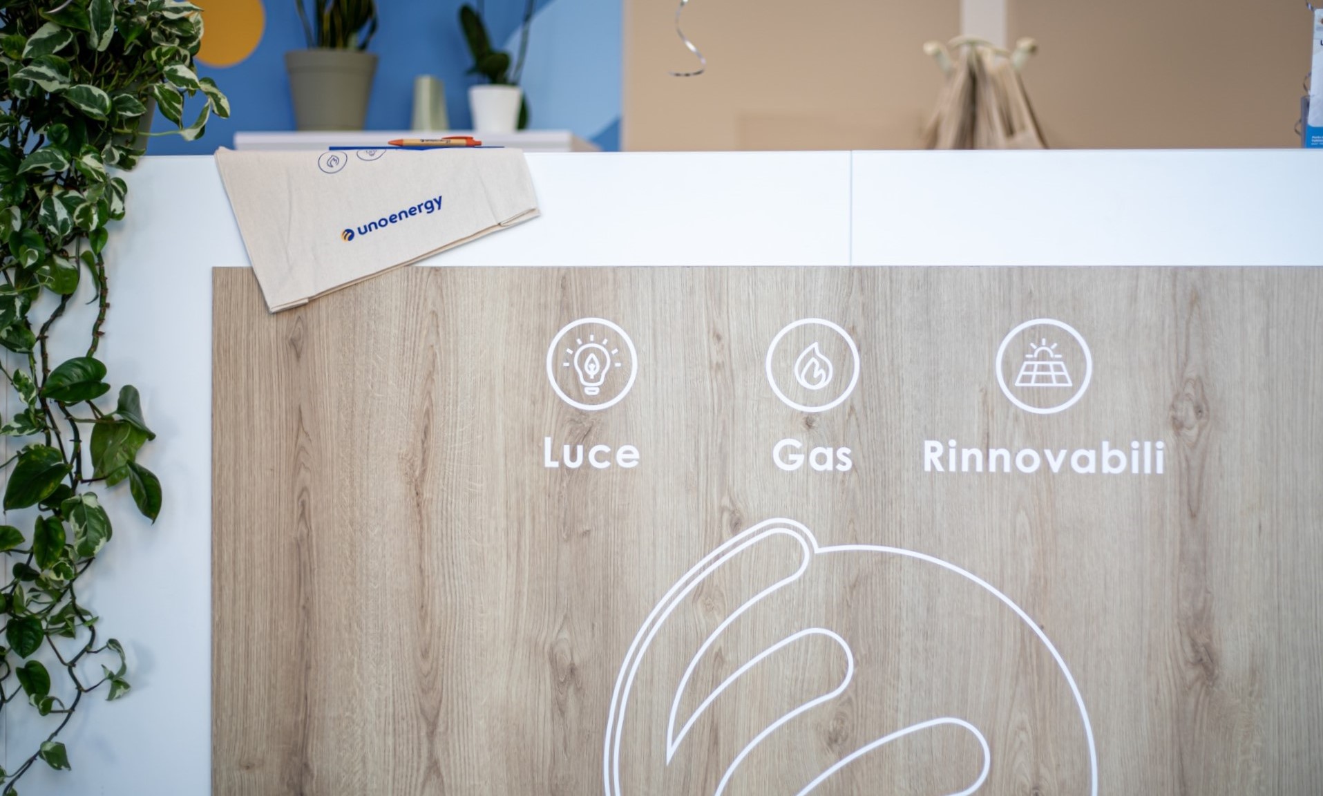 Rappresentazione grafica di Luce, Gas, Rinnovabili su pannello di legno con busta Unoenergy su ripiano.