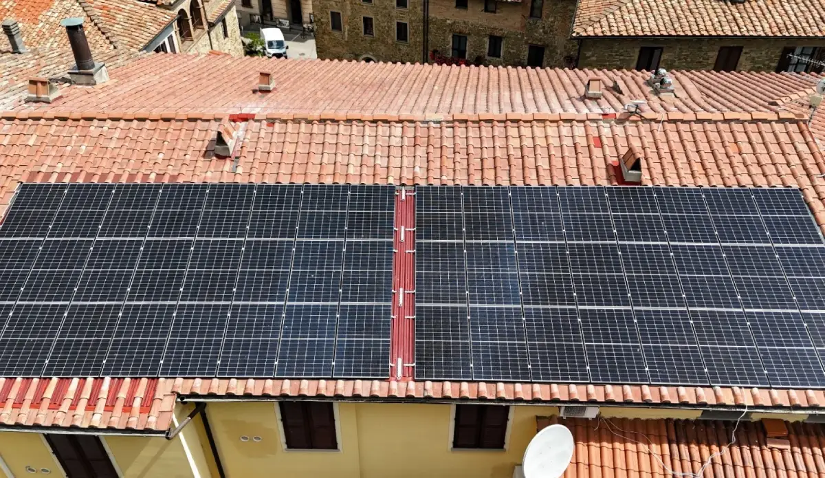 Pannelli solari su tetto di tegole rosse in un borgo storico con case in pietra.