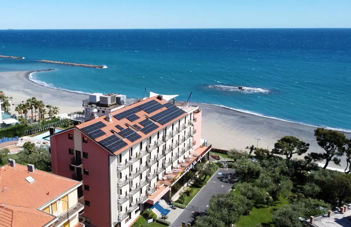 Edificio con pannelli solari fronte mare, vista spiaggia sabbiosa e vegetazione circostante.