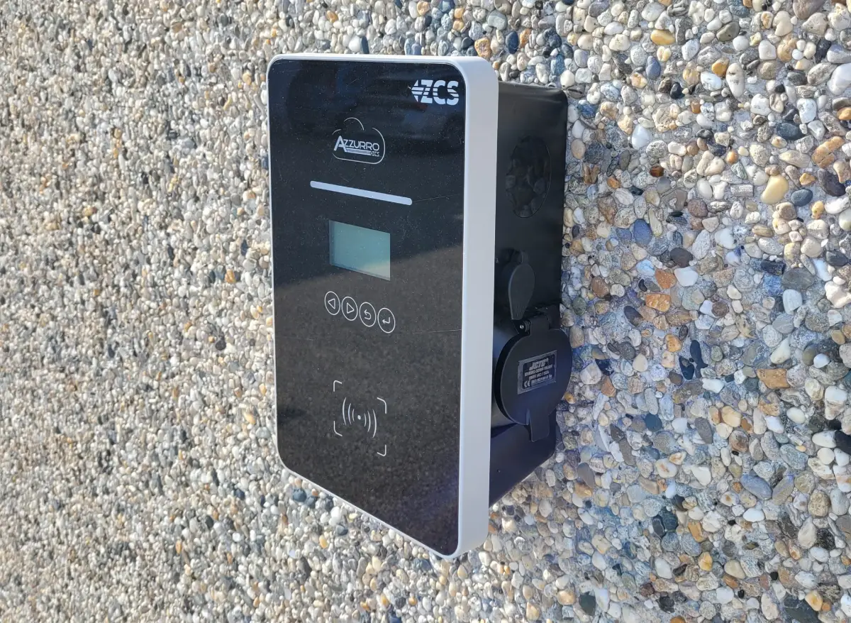 Caricabatterie Azzurro montato su un muro di ghiaia, schermo LCD e pulsanti di controllo visibili.