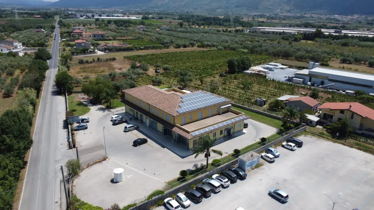 Edificio industriale con pannelli solari, parcheggio e vegetazione circostante, visto dall'alto.