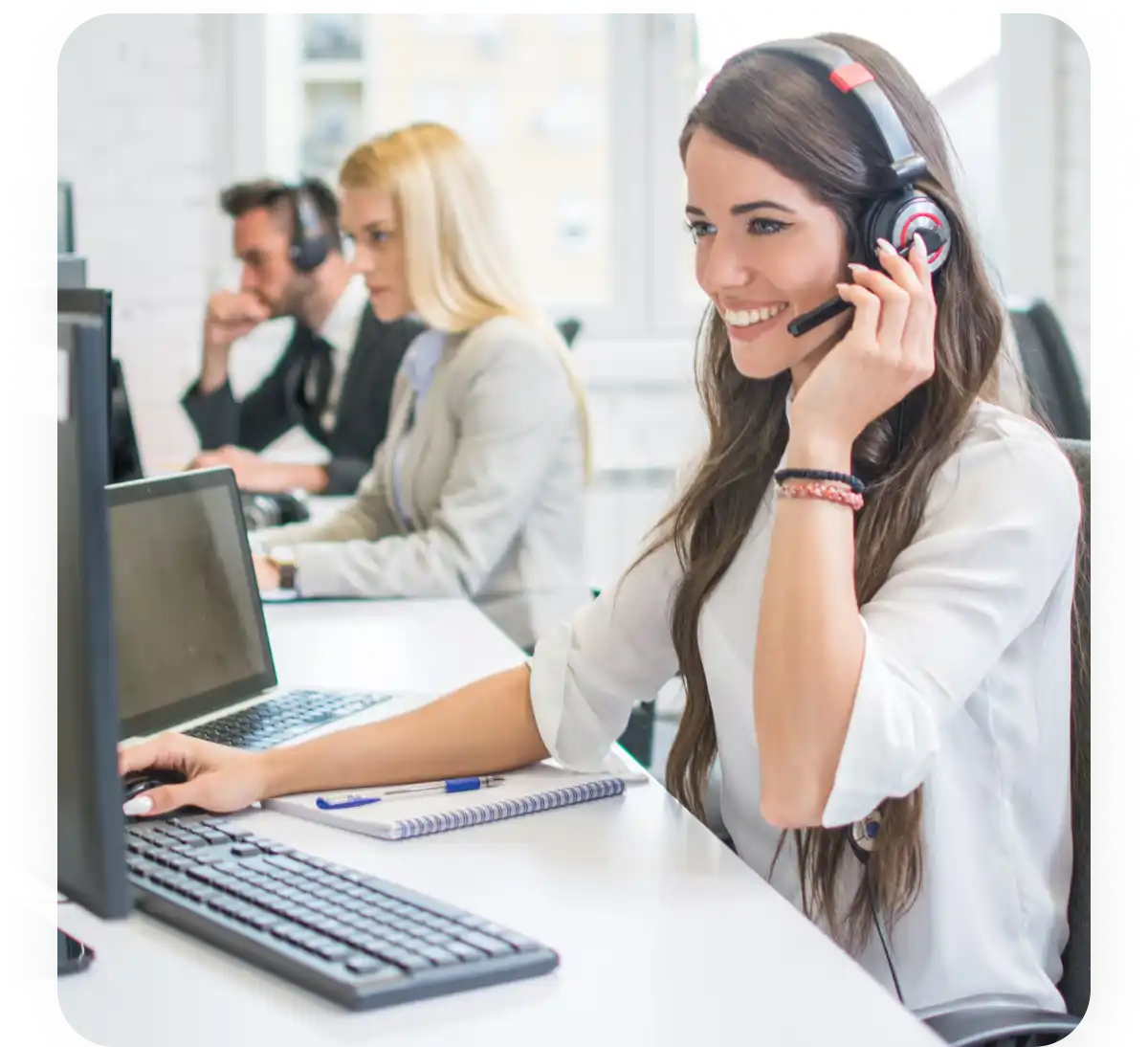 Operatore call center usa un computer e indossa un headset mentre lavora in ufficio con colleghi.