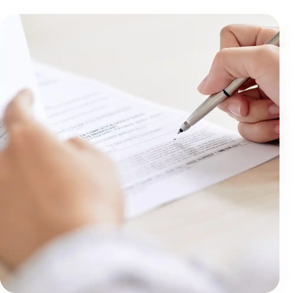 Mano che scrive su un documento con penna su un tavolo, focalizzata sulla compilazione del testo.