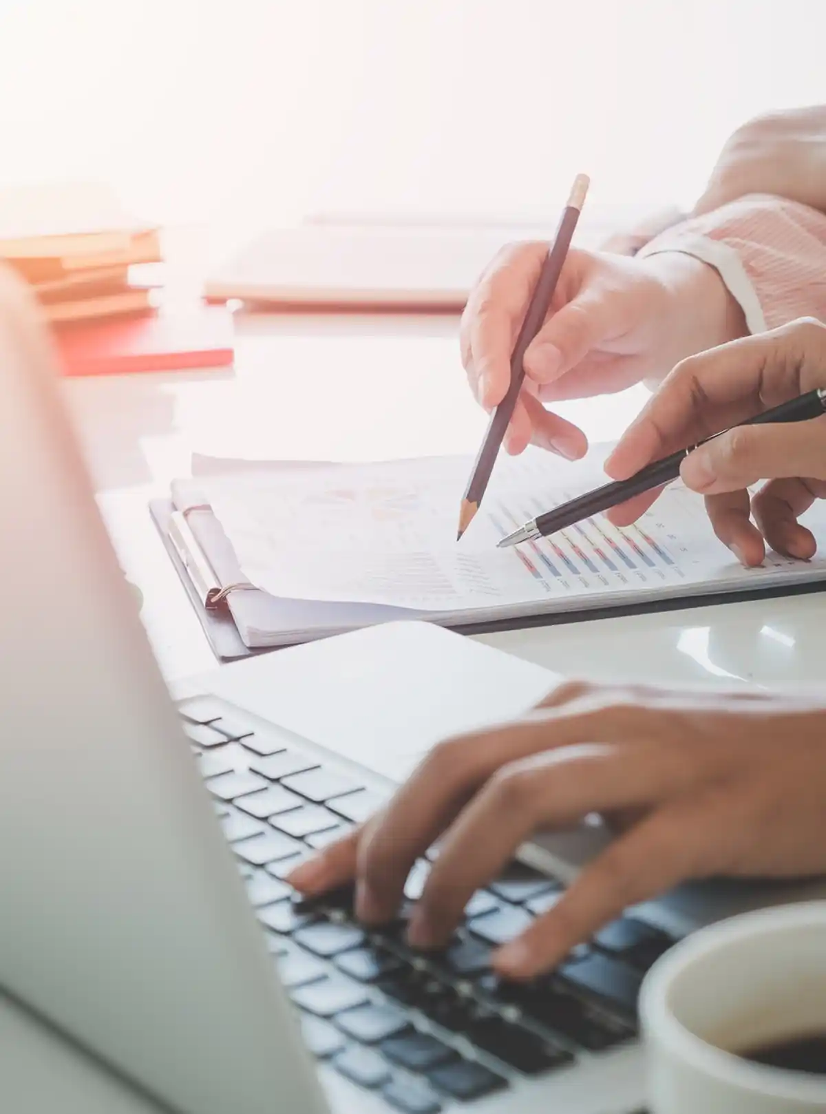 Persone lavorano a un laptop con grafici e documenti, discutendo analisi di dati in un ufficio luminoso.