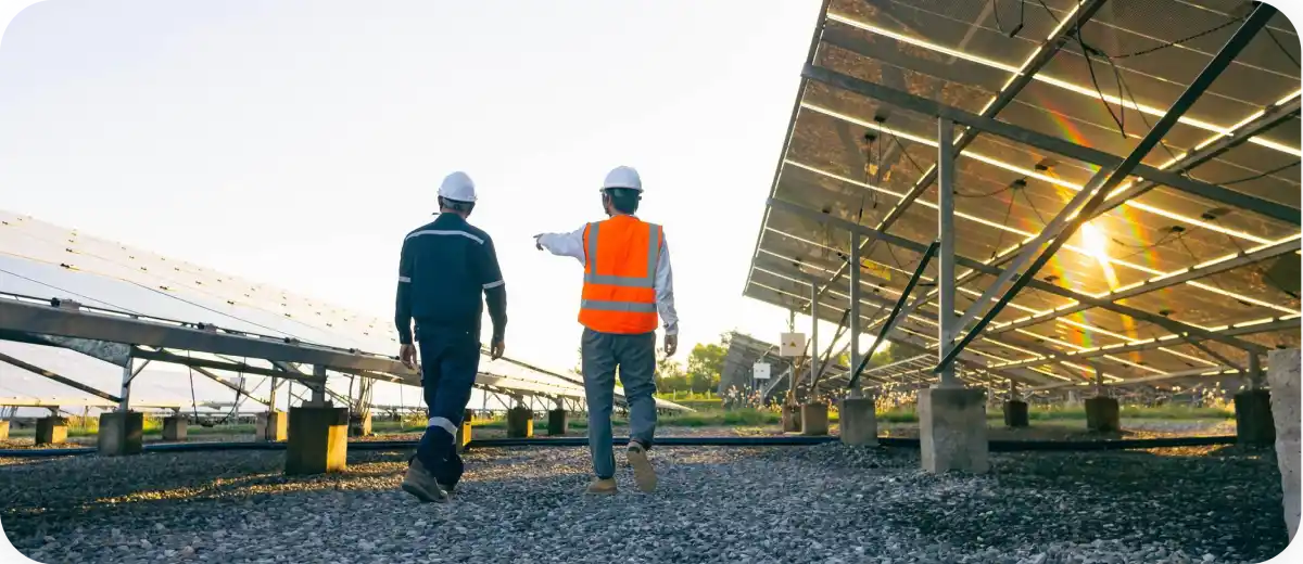 Due tecnici con elmetti camminano vicino a pannelli solari al tramonto.