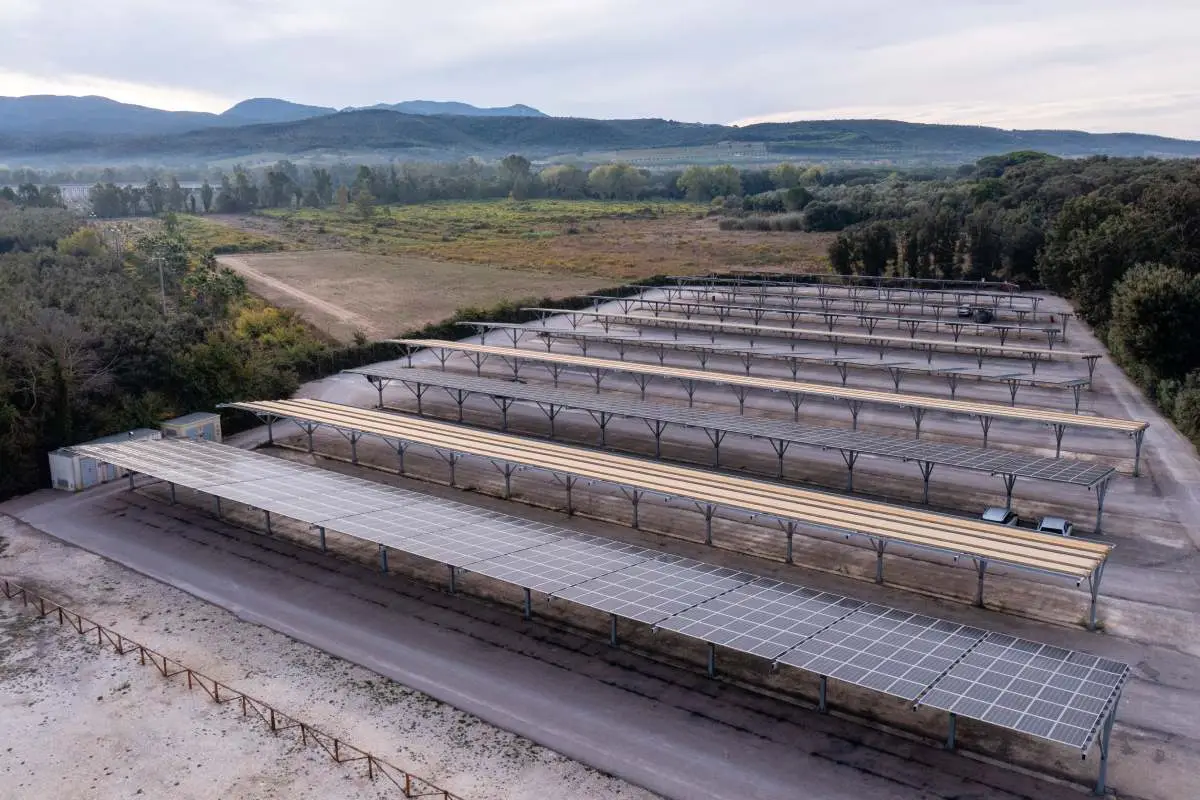 Parcheggio coperto con pannelli solari in campagna, vista aerea, colline sullo sfondo.