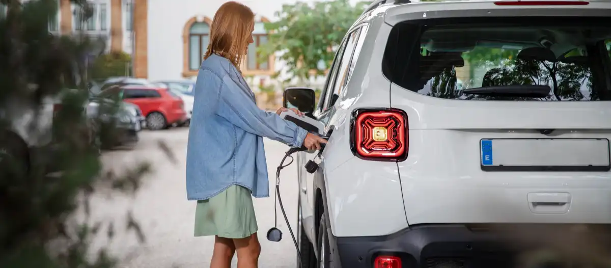 Donna carica SUV bianco elettrico in parcheggio residenziale con cavo di ricarica.