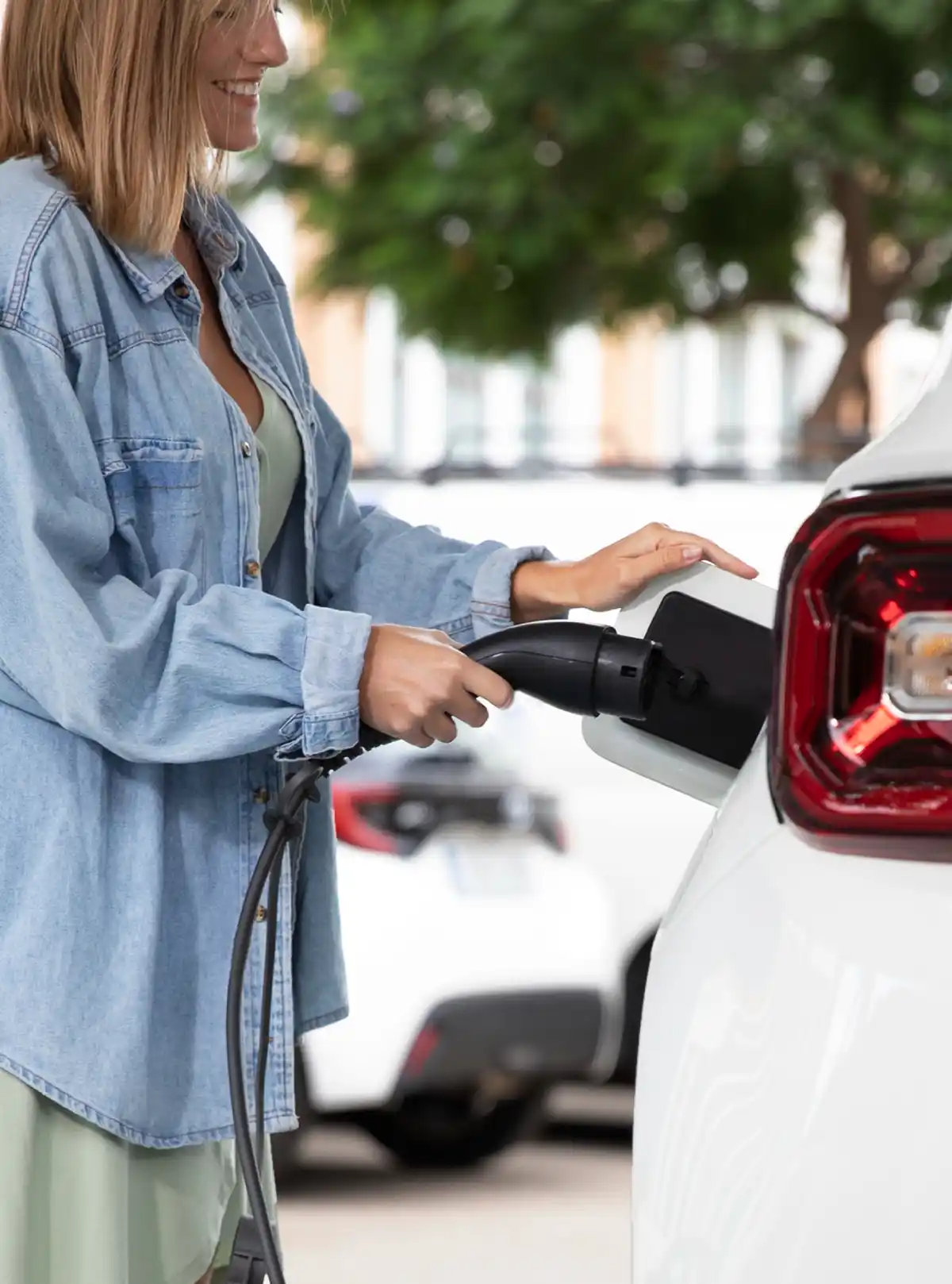 Donna ricarica un'auto elettrica bianca alla stazione di ricarica all'aperto.
