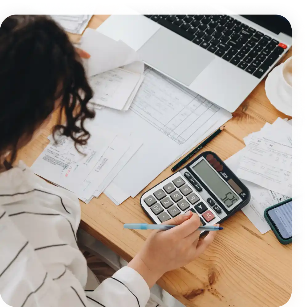 Donna lavora su contabilità al tavolo con calcolatrice, laptop e ricevute.